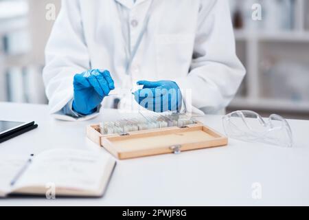 Ogni diapositiva ha una storia da raccontare. Primo piano di uno scienziato irriconoscibile che lavora con vetrini per microscopio da una scatola in un laboratorio Foto Stock