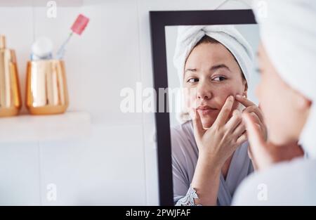 Schiacciare i pimples è genere di addictive. una bella giovane donna che analizza la sua pelle nello specchio del bagno Foto Stock