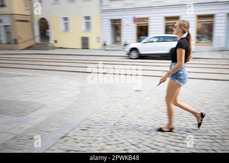 Donna cieca che cammina per le strade della città, utilizzando la sua canna bianca per navigare meglio lo spazio urbano e per raggiungere la sua destinazione in modo sicuro Foto Stock