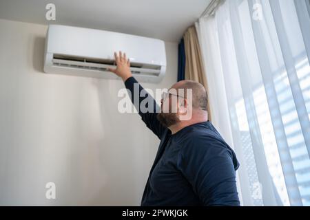 Uomo che controlla il funzionamento del condizionatore d'aria che tocca l'aria a mano nelle ore calde estive. Foto Stock
