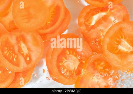 Fette di pomodoro in acqua su fondo bianco. Primo piano di pomodoro in liquido con bolle. Fette di pomodoro rosso maturo in acqua. Immagine macro di verdure in Foto Stock