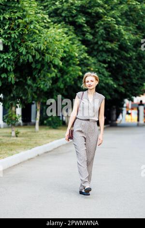 Ritratto lunghezza intera di buona donna che cammina all'aperto lungo il sentiero tra piante verdi. Ben vestito di mezza età, 40s signora. Spazio libero per la copia Foto Stock