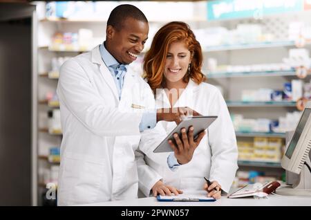 Gestire le attività in modo digitale. due farmacisti che lavorano insieme su un tablet digitale in un chimico Foto Stock