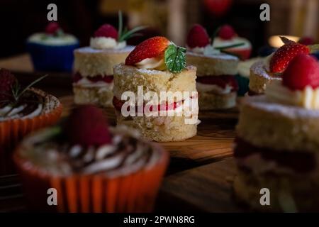 Belle mini spugne Victoria e cupcakes su taglieri di legno conditi Foto Stock