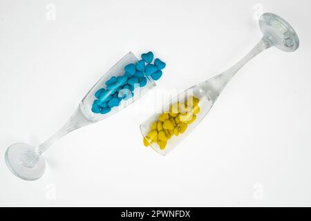 Due bicchieri rovesciato con caramelle a forma di cuore gialle e blu (primo piano) isolate su sfondo bianco. Simboli di Stato dell'Ucraina. Vista dall'alto Foto Stock