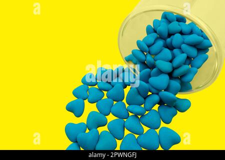 Vetro rovesciato con caramelle a forma di cuore blu (primo piano) isolate su sfondo giallo. Simboli di Stato dell'Ucraina. Vista dall'alto Foto Stock