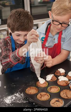 La glassa del ragazzo di scuola sui muffin con il sacchetto della glassa nella lezione domestica di economia, Baviera, Germania Foto Stock