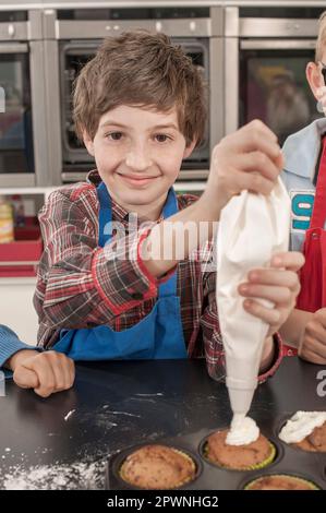 La glassa del ragazzo di scuola sui muffin con il sacchetto della glassa nella lezione domestica di economia, Baviera, Germania Foto Stock