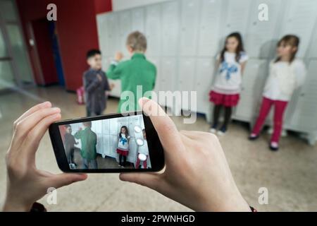 La mano della persona filma due scolari che combattono nel corridoio scolastico con il telefono cellulare, Baviera, Germania Foto Stock