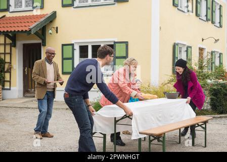 Famiglia preparare un tavolo da picnic all'esterno in casa colonica, Baviera, Germania Foto Stock