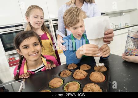 La glassa del ragazzo di scuola sui muffin con il sacchetto della glassa nella lezione domestica di economia, Baviera, Germania Foto Stock