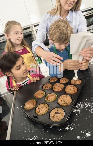 La glassa del ragazzo di scuola sui muffin con il sacchetto della glassa nella lezione domestica di economia, Baviera, Germania Foto Stock