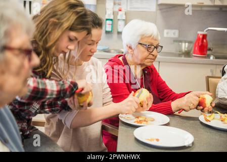 Donne anziane con ragazze che sbucciano la mela a casa di riposo Foto Stock