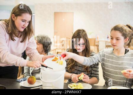 Donna anziana con ragazze che pelano la mela a casa di riposo Foto Stock