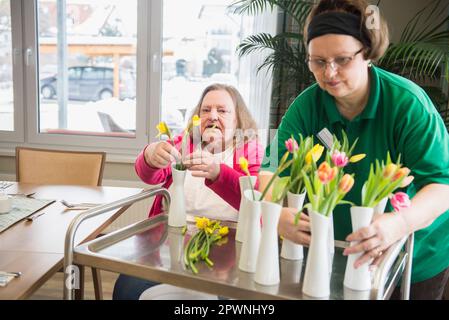 Custode e donna anziana che organizza fiori e vasi a casa di riposo Foto Stock