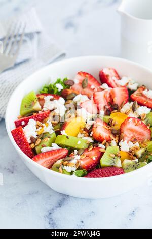 Insalata di frutta con feta e semi in una ciotola bianca su un tavolo bianco. Sana ricetta estiva vegana detox. Foto Stock