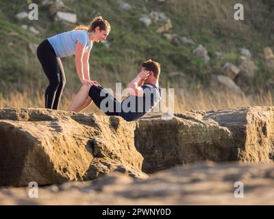 Donna che tiene le gambe dell'uomo che fa le scricchiolature all'aperto Foto Stock