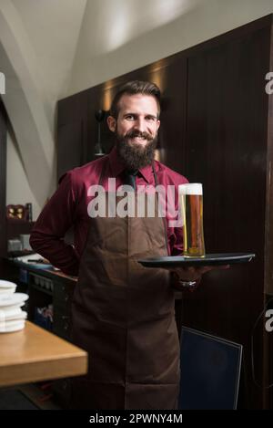 Ritratto del manager sorridente che porta un bicchiere di birra grande sul vassoio Foto Stock