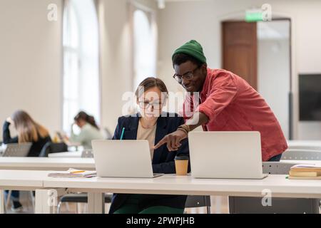 Un ragazzo afroamericano aiuta le studentesse caucasiche a lavorare su un progetto nell'università universitaria. Foto Stock