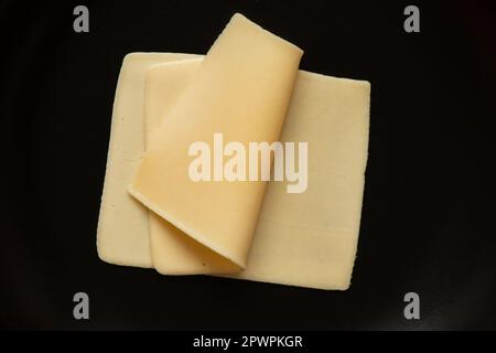 Fette di formaggio duro giacciono su un piatto nero primo piano, cibo Foto Stock