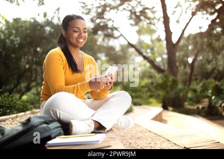 Felice donna che si rilassa nel parco con smartphone, navigando in internet e chattando nei social network all'aperto Foto Stock