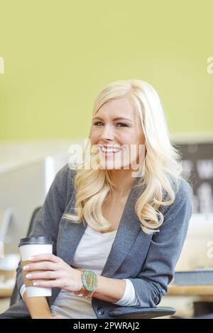 Ritratto di una giovane bella donna d'affari bionda seduta su una sedia e bere caffè in un ufficio al lavoro. Un'azienda femminile allegra Foto Stock
