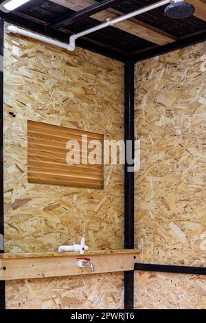 Cabina doccia estiva con telaio in tubi profilati metallici, rivestita con pannelli OSB, con rubinetto e soffione doccia interno. Foto Stock