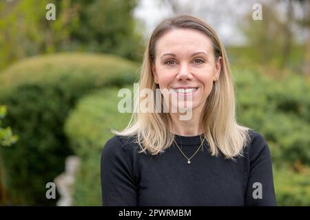 Bella donna bionda nella sua 40s indossando una camicia nera e collana sorride piacevolmente alla macchina fotografica Foto Stock