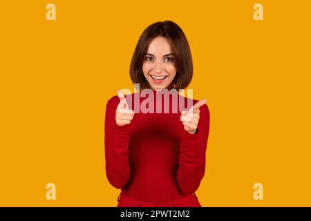 Ragazza bruna allegra e simpatica che indica la macchina fotografica Foto Stock