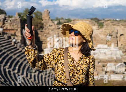 Un turista asiatico vietnamita che indossa un cappello e occhiali da sole utilizza una videocamera per visitare il grande e ben conservato anfiteatro romano di si Foto Stock