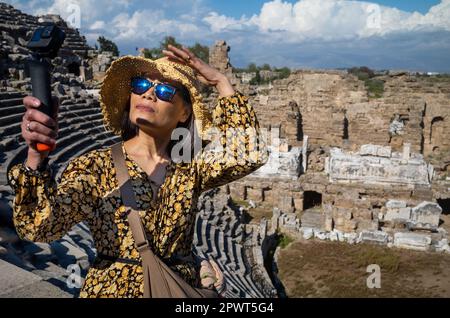 Un turista asiatico vietnamita che indossa un cappello e occhiali da sole utilizza una videocamera per visitare il grande e ben conservato anfiteatro romano di si Foto Stock