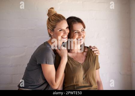 Condividere una risata con il suo testicolo. due giovani donne simpaticose che ridono seduti in uno studio. Foto Stock