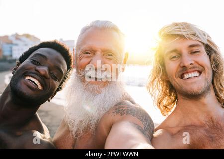 Amici multigenerazionali felici che prendono selfie sulla spiaggia - amici maschili multirazziali che si divertono durante le vacanze estive - stile di vita di viaggio di vacanza Foto Stock