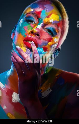 Il colore è potente e influenza direttamente l'anima. Studio shot di una giovane donna che posa con vernice multicolore sul suo viso Foto Stock