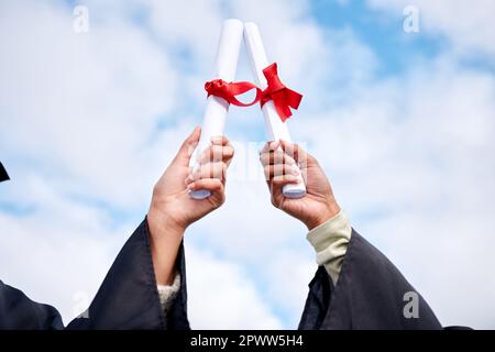 Guarda noi conquistare con le nostre chiavi per il futuro. Primo piano di due donne irriconoscibili che festeggiano con i loro diplomi il giorno della laurea Foto Stock