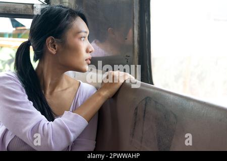 Una giovane donna siede su un vecchio autobus e guarda indietro attraverso il finestrino posteriore Foto Stock