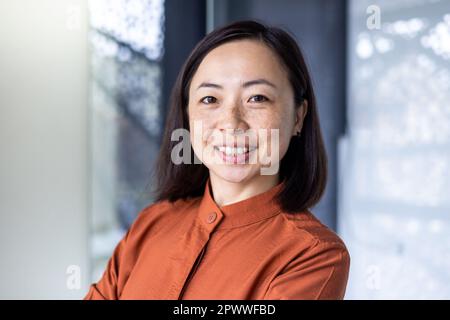 Ritratto di giovane bella e di successo donna asiatica d'affari, donna dipendente sorridente e guardando la macchina fotografica con braccia incrociate, donna finanziaria soddisfatto dei risultati del suo lavoro. Foto Stock