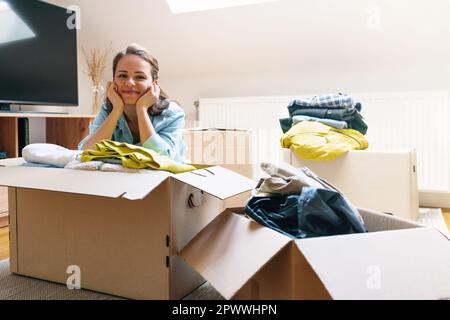 Giovane donna di brunette che le confezionava i vestiti in scatole di cartone a casa. Foto Stock