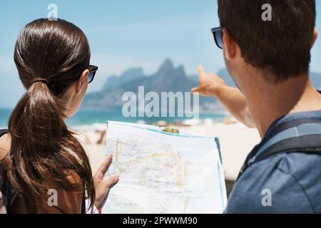 Credo che l'albergo sia tornato così. una giovane coppia che guarda una mappa mentre è in piedi su una spiaggia Foto Stock