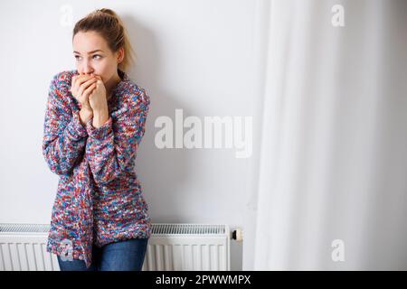 Donna fredda, depressa di mezza età a casa sentirsi triste, solitario, ansioso per i prezzi dell'energia in aumento (immagine dai toni del colore) Foto Stock