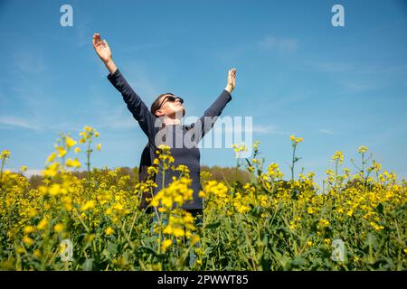 Donna in piedi in un campo giallo con le braccia sollevate, mente spirito corpo concetto. Foto Stock