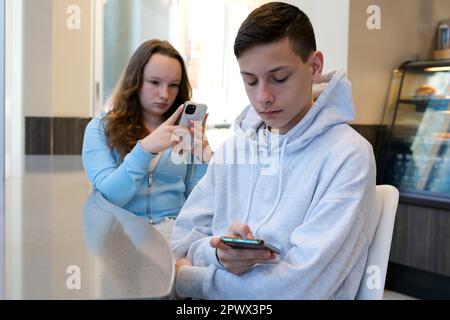 Annoiato attraente donna che guarda stanco, mentre il suo ragazzo utilizza uno smartphone per registrare una breve storia per i social media adolescenti su una data tenere i telefoni nelle loro mani sono impegnati in social network Foto Stock