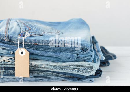 Pila di jeans blu e tag vuoto su sfondo bianco Foto Stock