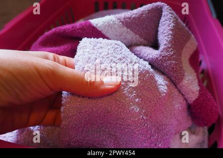 La mano di una donna sente un asciugamano di cotone colorato da un cesto con bucato sporco. Lavanderia selezione e lavaggio. Lavanderia o bagno. Servizio di pulizia Foto Stock