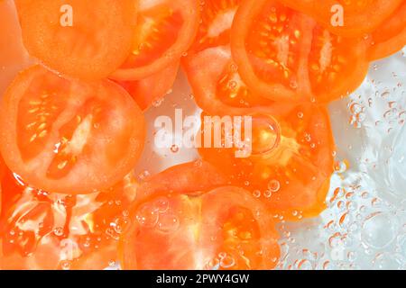 Fette di pomodoro in acqua su fondo bianco. Primo piano di pomodoro in liquido con bolle. Fette di pomodoro rosso maturo in acqua. Immagine macro di verdure in Foto Stock