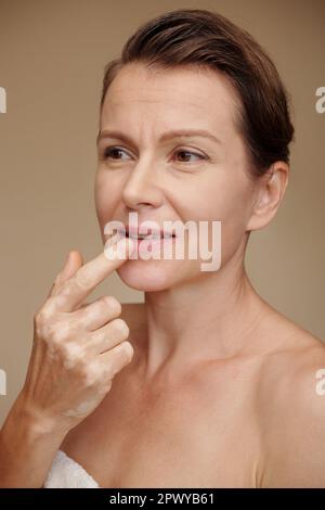 Ritratto di donna matura che applica balsamo nutriente sulle labbra Foto Stock