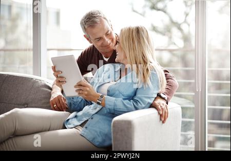 La felicità è una sensazione condivisa al meglio. una coppia matura che utilizza un tablet digitale mentre si rilassa insieme sul divano di casa Foto Stock