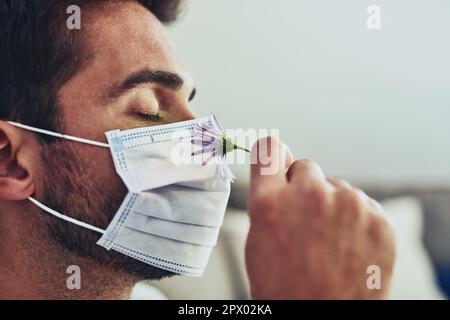 Ora posso sentire l'odore dei fiori mentre indosso la protezione. Primo piano di un uomo allegro e irriconoscibile che indossa una maschera protettiva e che odora gli occhi di un fiore chiusi Foto Stock