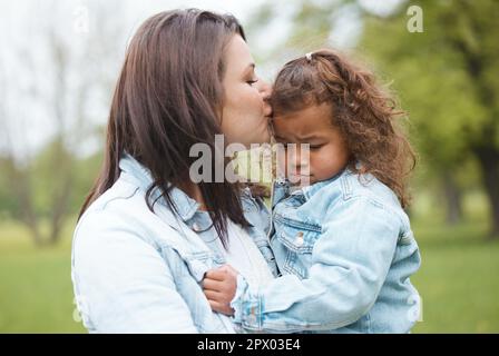 Amore, parco e madre baciano il bambino con l'espressione sconvolta, triste e infelice sul viso per lasciare il parco giochi. Famiglia, sostegno e mamma baciare la giovane ragazza per Foto Stock