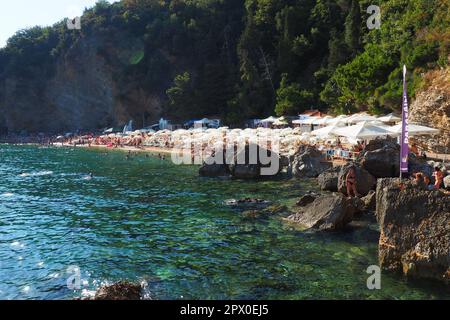 Budva, Montenegro, spiaggia di Mogren. Agosto 15 2022 Spiaggia di sabbia e ciottoli vicino a alte scogliere. Ombrelloni, caffè, sedie a sdraio, sdraio. Le persone si rilassano Foto Stock